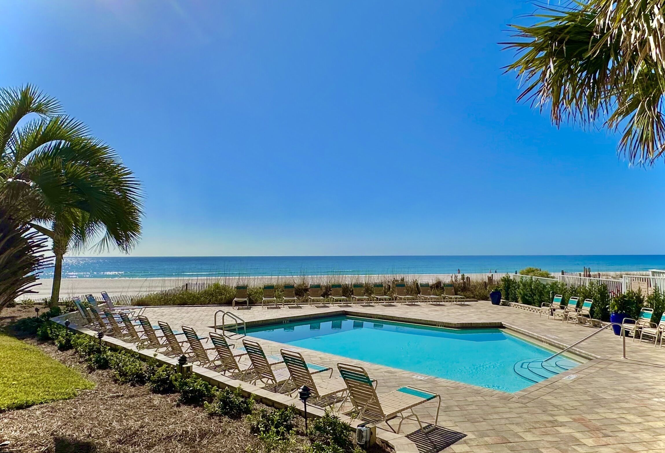 A pool area with lounge chairs and a view of the ocean.