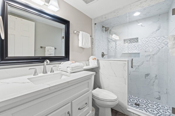 Un bagno moderno con un grande specchio, due lavabi, un water e una cabina doccia con piastrelle decorate.