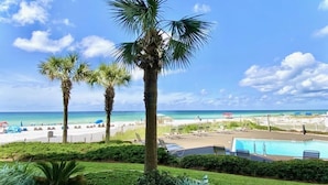 Zona de piscina con sillones, palmeras y vista a la playa y al océano.