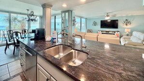 A spacious living area with a large island kitchen, a flat-screen TV, and a balcony with a view of the ocean. - Cozy Condo in PCB! FREE Beach Chairs! PW 212 (Panama City Beach)