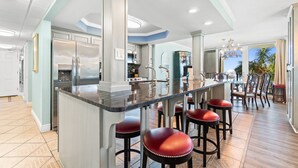 A spacious kitchen with a central island, bar stools, and a view of the outdoors. - Cozy Condo in PCB! FREE Beach Chairs! PW 212 (Panama City Beach)