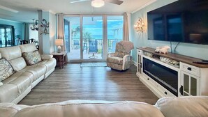 A living room with a sofa, a chair, a TV, and a balcony with a view. - Cozy Condo in PCB! FREE Beach Chairs! PW 212 (Panama City Beach)