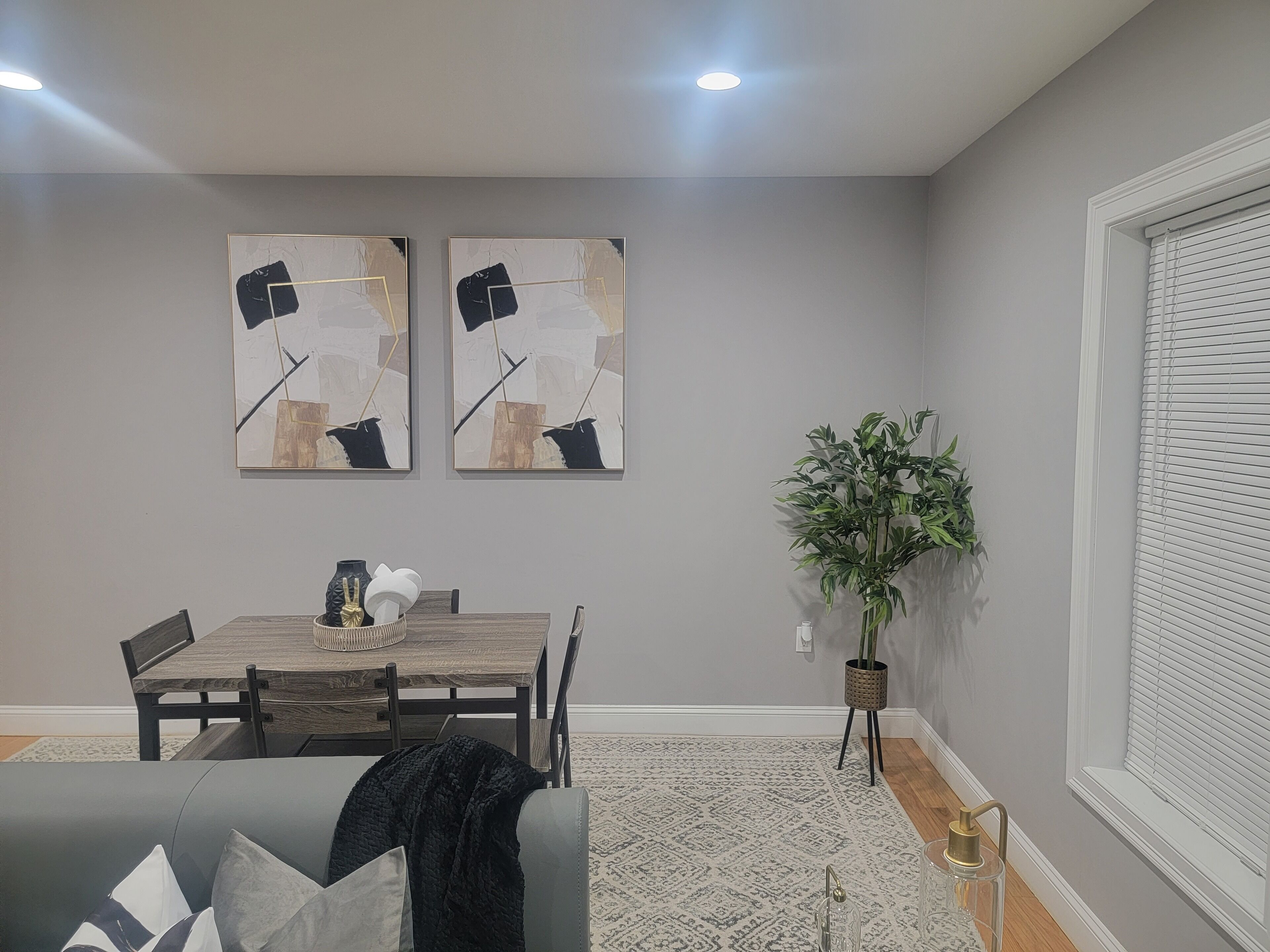 A dining area with a wooden table and chairs, a gray couch, and two abstract paintings on the wall.