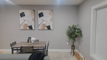 A dining area with a wooden table and chairs, a gray couch, and two abstract paintings on the wall.