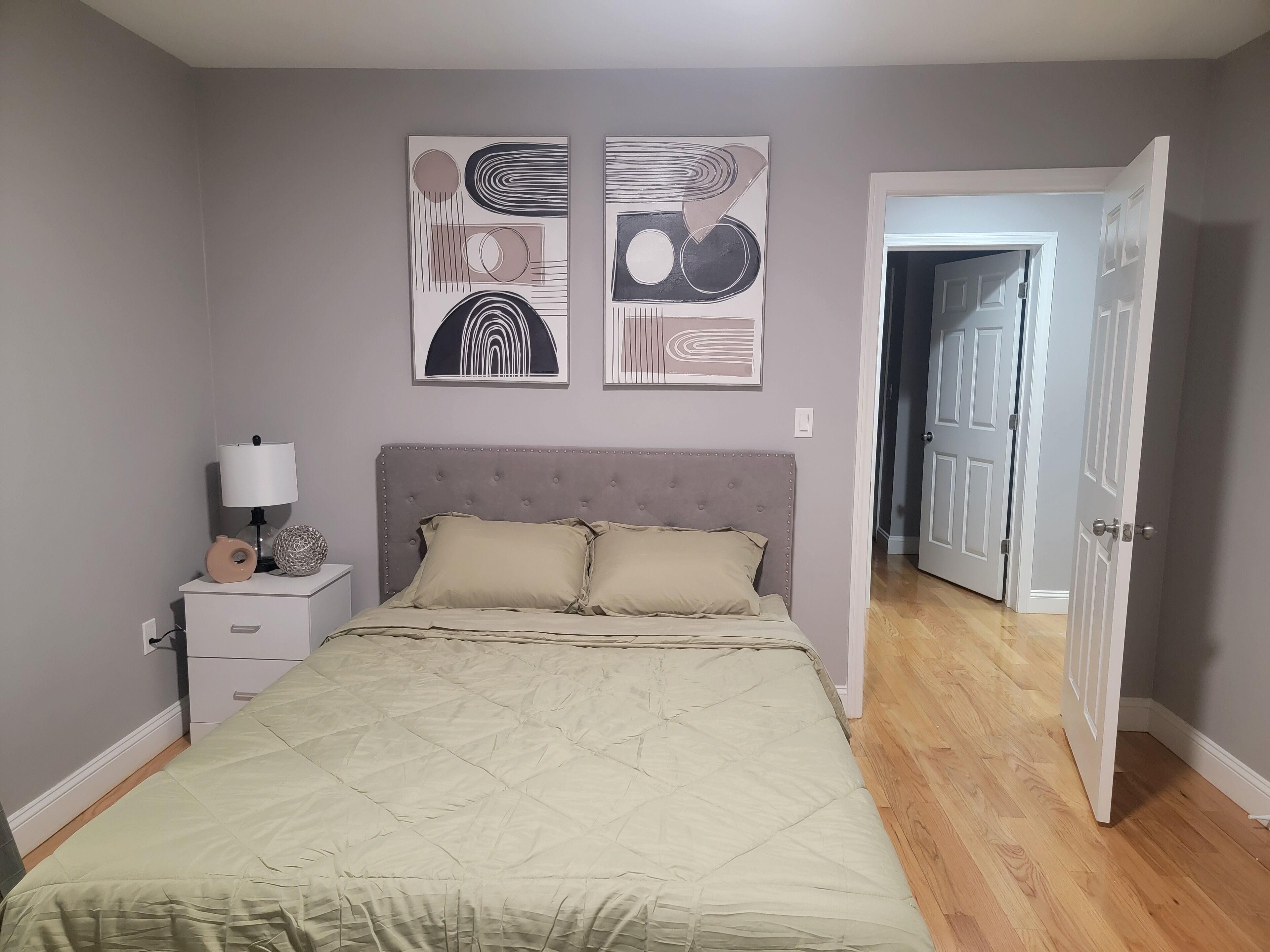 A bedroom with a bed, bedside table, lamp, and two abstract wall art pieces.