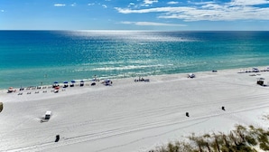 Une plage de sable blanc, avec une eau d’un bleu limpide et quelques parasols.