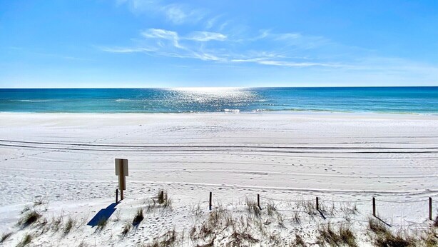 Ein Strand mit blauem Himmel, sandigem Ufer und einem Holzschild im Vordergrund.