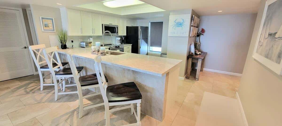 Una cocina moderna con una isla central, armarios blancos y un comedor con sillas blancas.