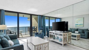 Uma sala de estar ampla com varanda e vista para o mar, mobiliada com sofá, poltrona e mesa de centro.