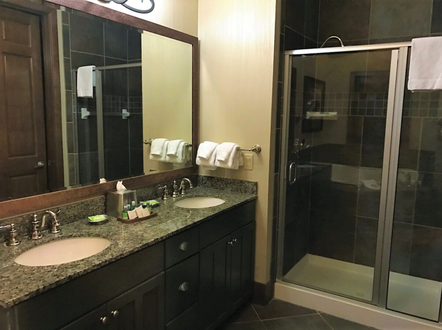 Une salle de bain d’hôtel avec un double lavabo, un grand miroir et une douche à parois de verre.