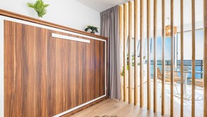 Een kamer met een houten kledingkast, een geweven vloerkleed en uitzicht op een balkon met buitenmeubilair.