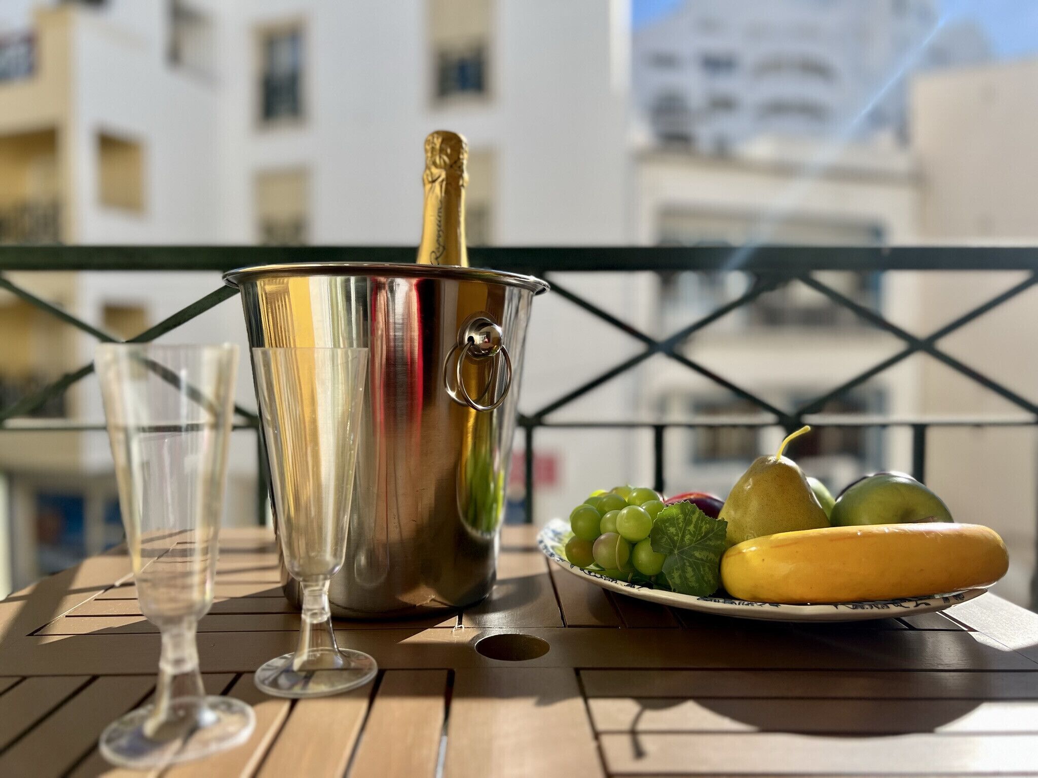 Een balkon met een eettafel, inclusief een fruitschaal en een fles champagne.