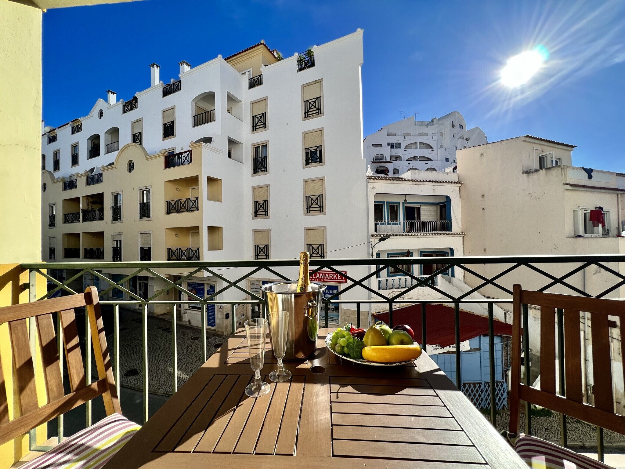 A balcony with a table set with a bottle of champagne, glasses, and a fruit bowl.