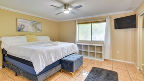 Una camera da letto con un letto, un ventilatore a soffitto, una TV e una finestra con tende.