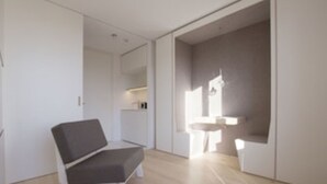 A modern, minimalistic room with a grey sofa, a small white table, and a built-in sink. - Wohneinheit 3594848 (Zorneding)