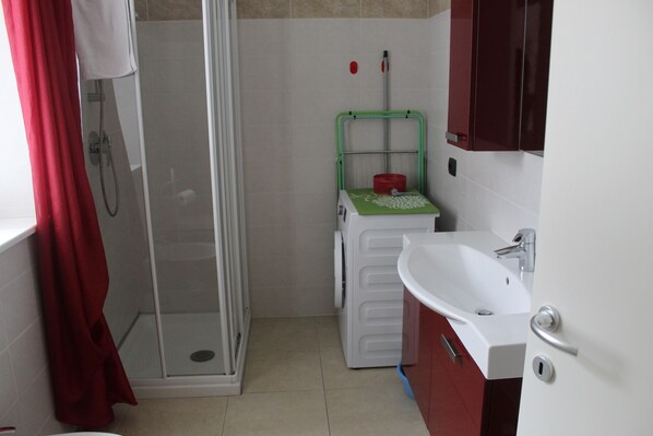 Un baño pequeño con cabina de ducha de vidrio, lavadora y lavamanos.