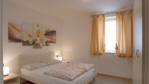 Un dormitorio con dos camas, una mesita de noche, una lámpara y una ventana con cortinas.