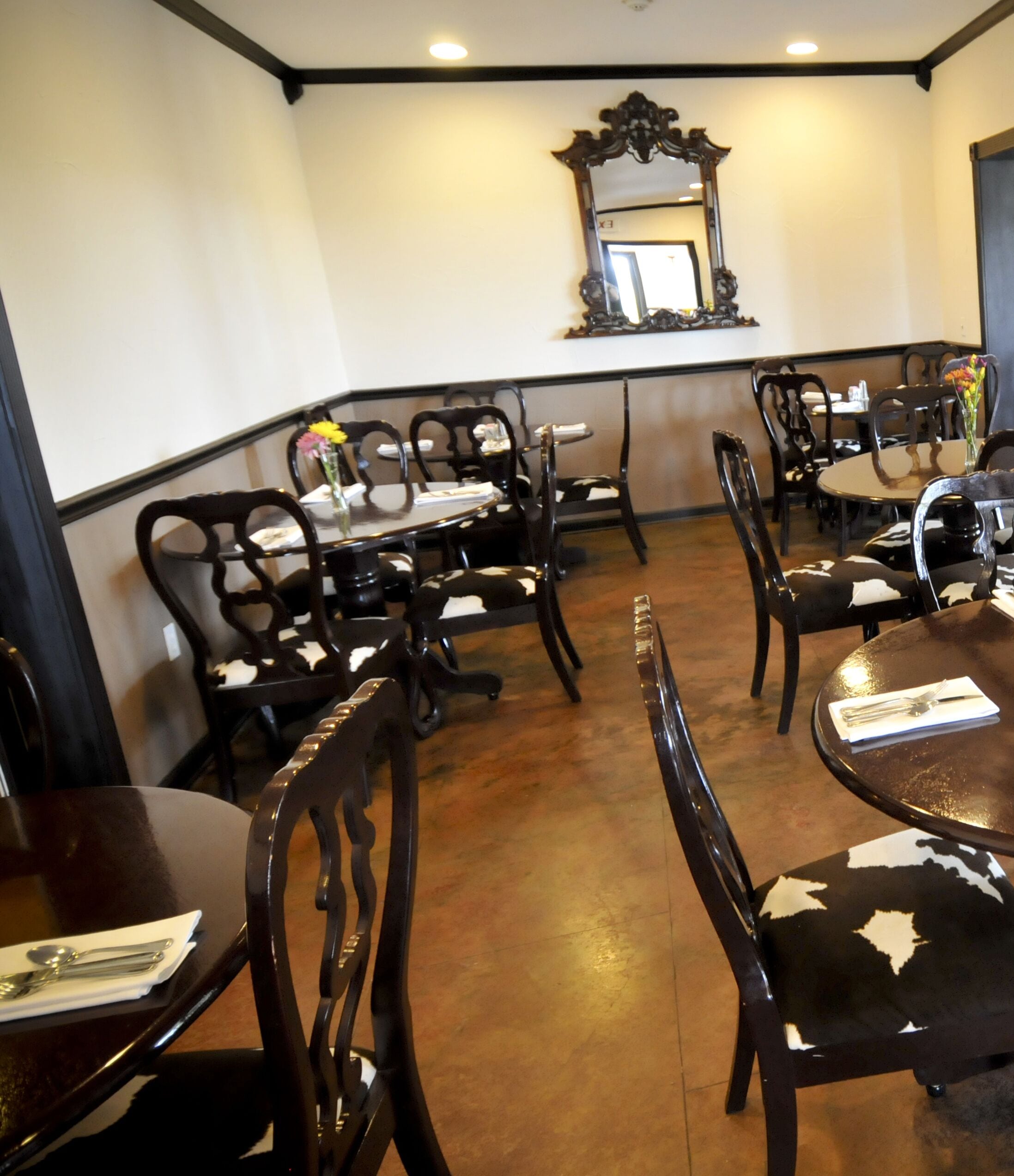 A dining area with round tables and chairs, a mirror on the wall, and a tiled floor.