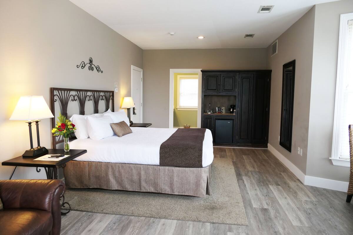 A hotel room with a large bed, two bedside tables with lamps, a chair, a desk, and a small table with a vase of flowers.