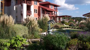 Ein großes, zweistöckiges Gebäude mit Balkonen und einem angelegten Garten mit Brunnen und unterschiedlichen Pflanzen.
