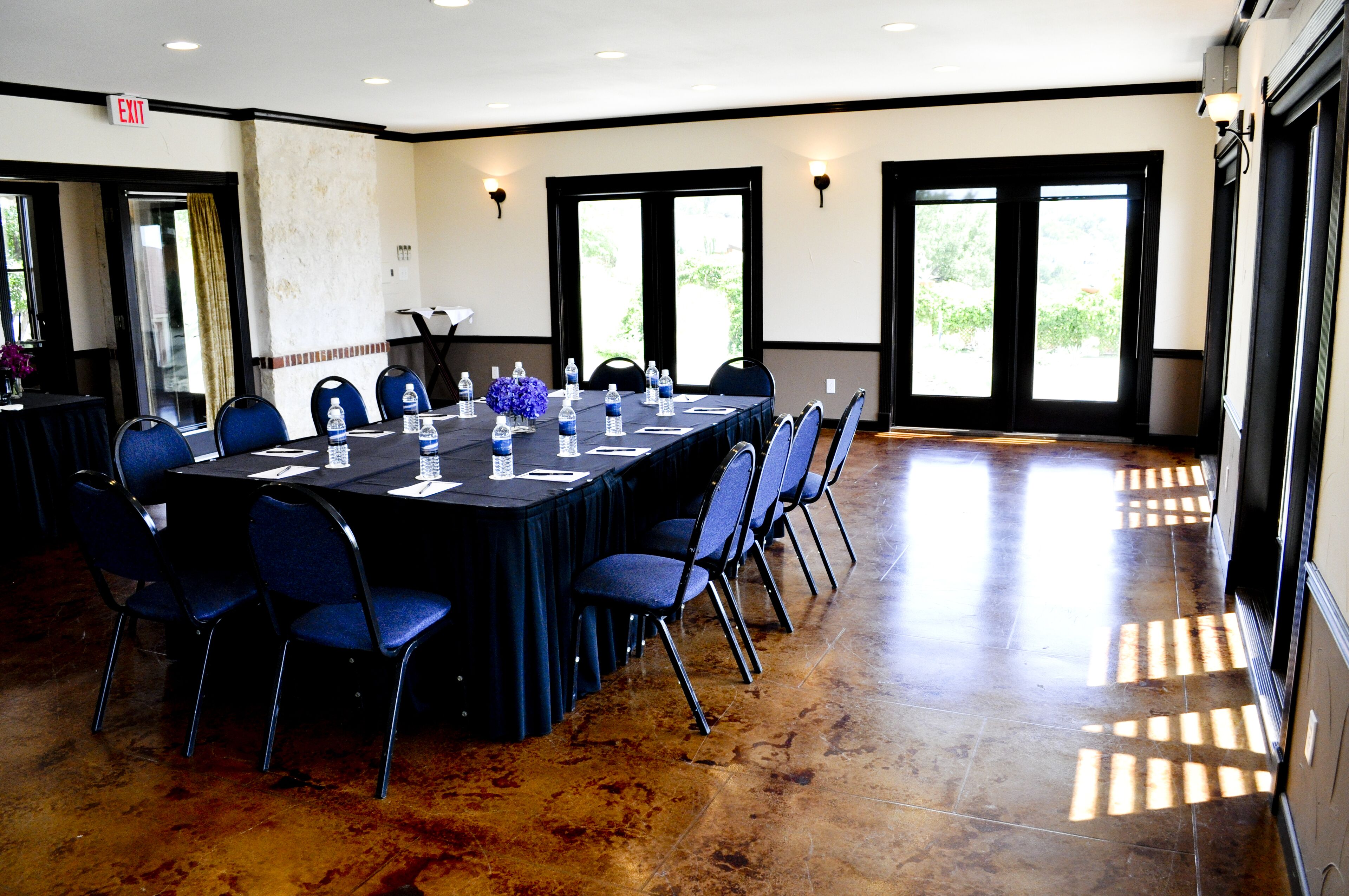Un salón de conferencias con una larga mesa, sillas, botellas de agua y un jarrón de flores.