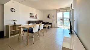 A modern living room with a dining area, a sofa, a coffee table, and a large window with a view. - V019 - Mestral 1 (Roses)