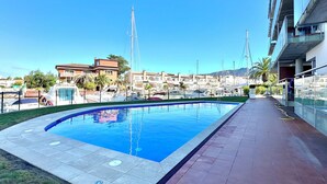 A swimming pool with a tiled deck, surrounded by buildings and a clear sky. - V019 - Mestral 1 (Roses)