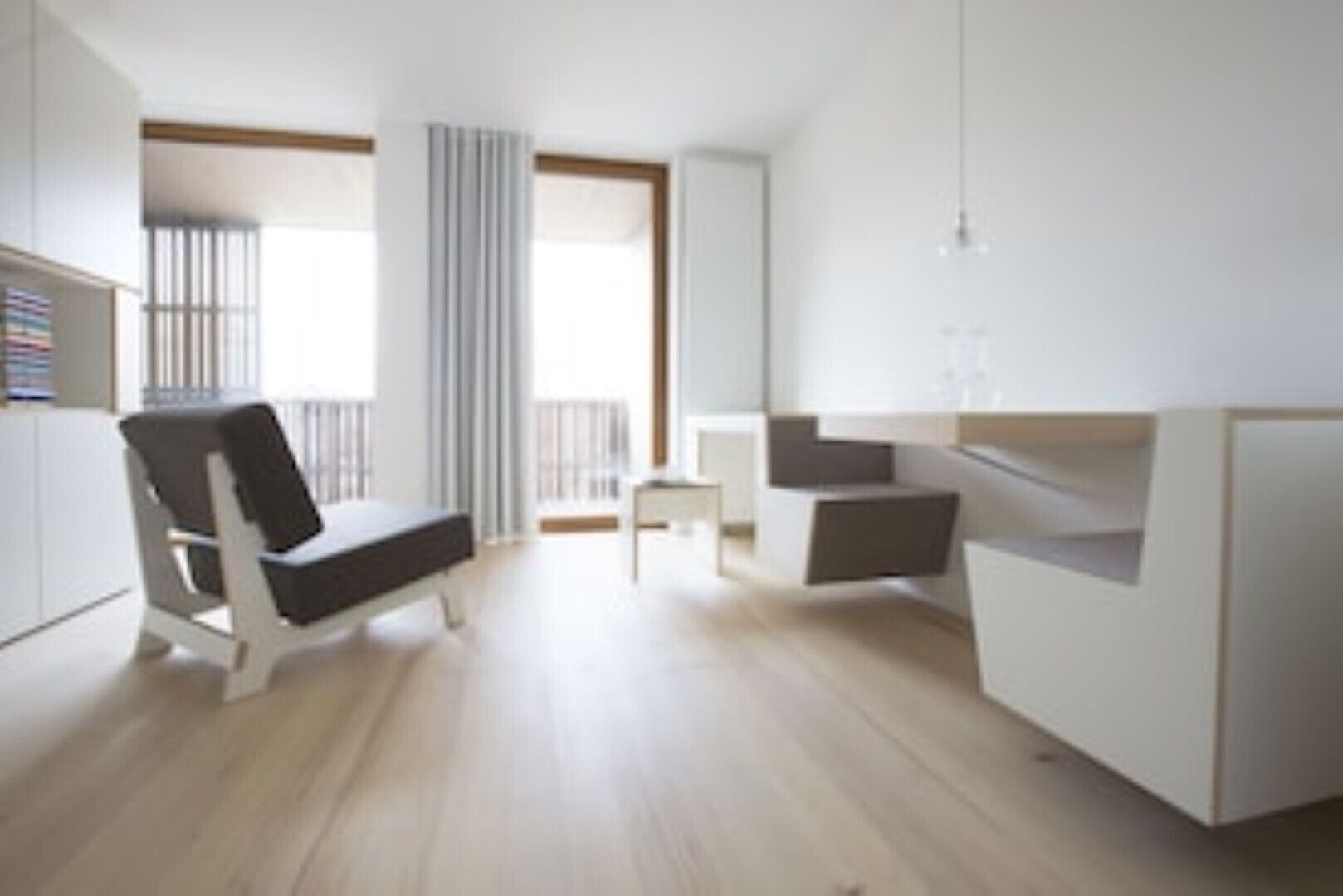 Ein moderner, minimalistischer Raum mit einem Bett, einem Sessel und einem kleinen Tisch.