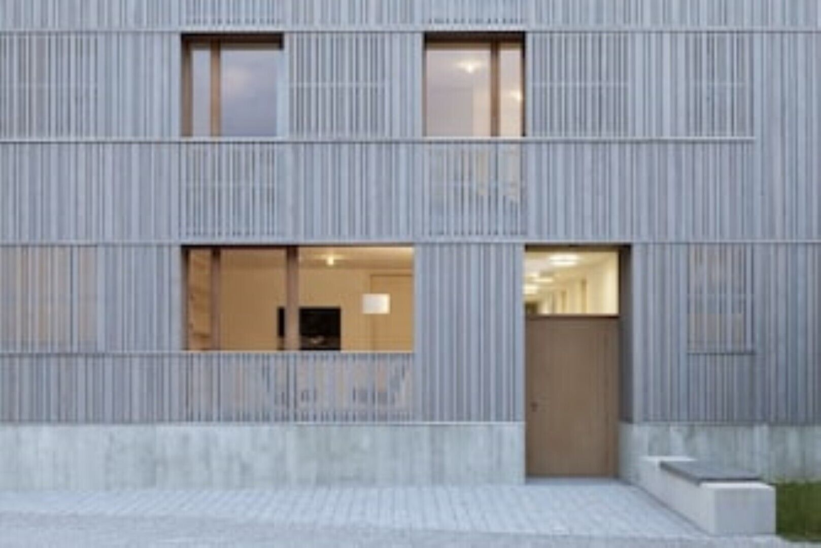 Un bâtiment moderne avec une façade en métal ondulé, de grandes fenêtres et une base en béton.
