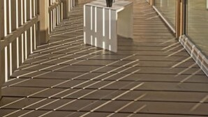 Ein moderner Balkon mit Holzbelag, einem weißen Tisch und Geländer aus Glas.
