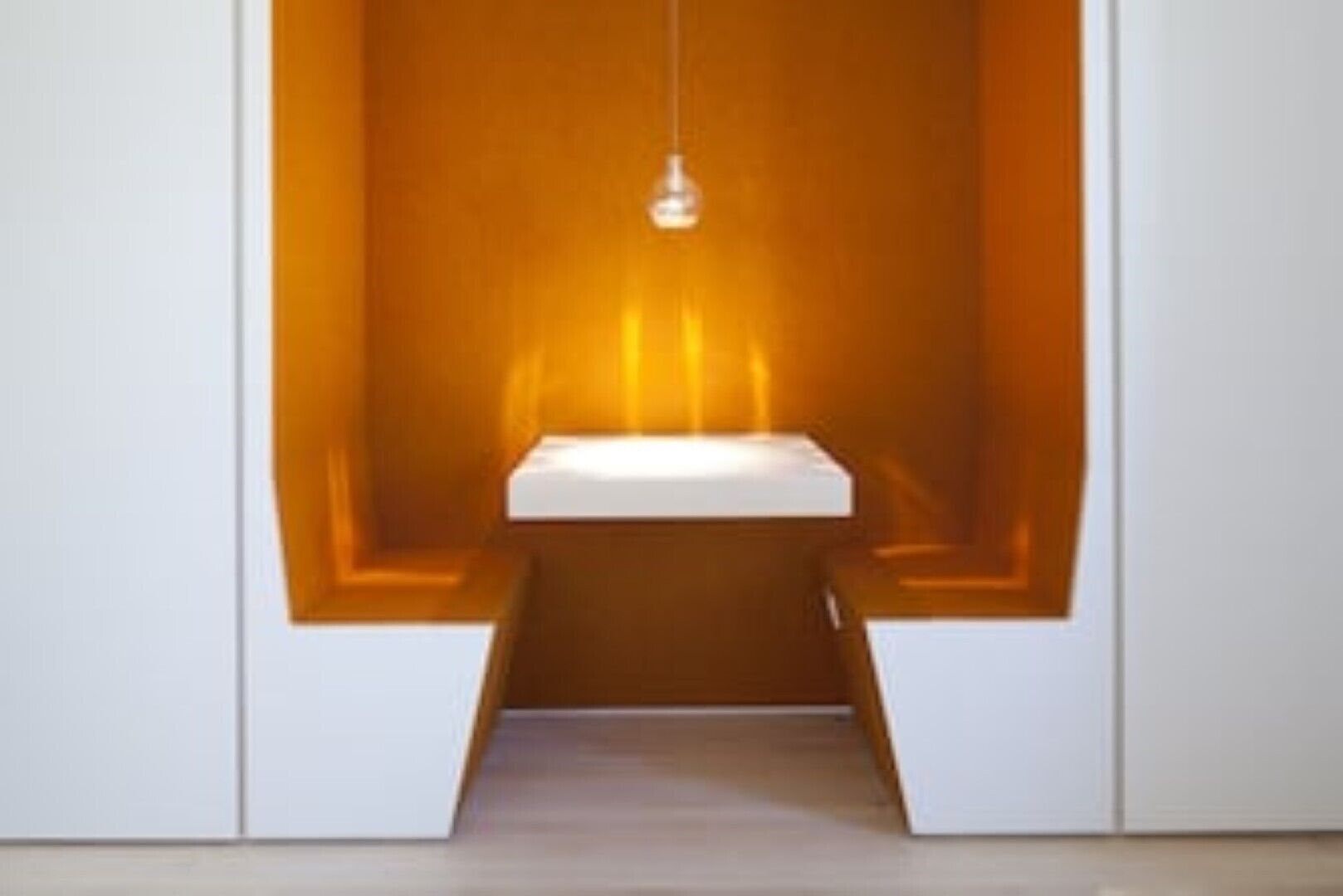Un baño minimalista con un lavamanos blanco y una lámpara colgante.