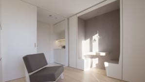 Ein modernes, minimalistisches Zimmer mit grauem Sofa, kleinem weißen Tisch und integriertem Waschbecken.