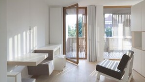 Ein modernes, minimalistisches Zimmer mit einer großen Schiebeglasdoor zum Balkon, einer Couch und einem kleinen Tisch.