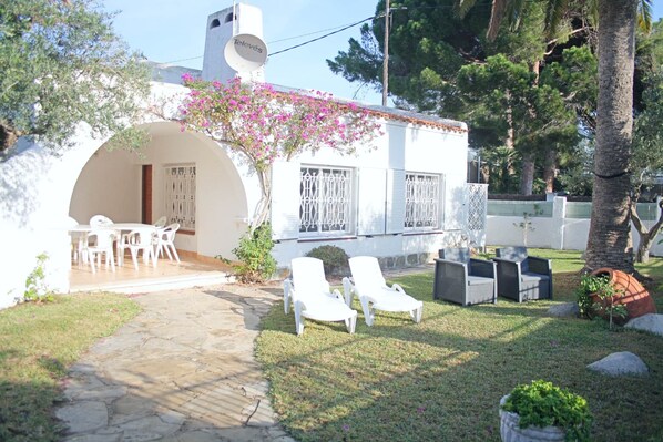 Une villa blanche dotée d’un patio couvert, d’un espace salon extérieur et d’un jardin agrémenté d’un palmier.