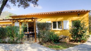 Un edificio amarillo con techo de tejas, un patio cubierto y un jardín con plantas y rocas.