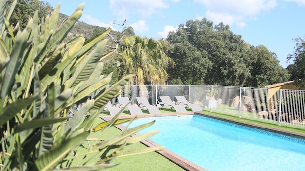 Piscina con sillas de descanso y un área cercada, rodeada de vegetación y árboles.