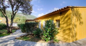 Un edificio amarillo con tejado de baldosas, rodeado de vegetación y un sendero.