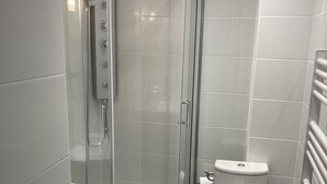A modern bathroom with a glass-enclosed shower, a white toilet, and a wooden floor.