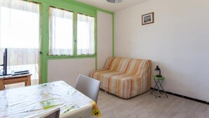 A room with a bed, a small table, a chair, a striped sofa, a lamp, and a picture on the wall.
