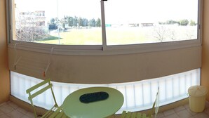 A corner room with a window overlooking a sports field, a small table with a chair, and a radiator.