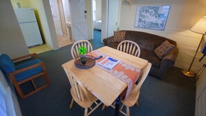 Een gezellige, compacte ruimte met een eettafel, stoelen, een bank en een kleine keuken met een koelkast.