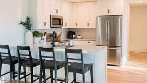 A modern kitchen with white cabinets, stainless steel appliances, and a central island with bar stools. - Newly renovated modern & spacious home complete with a private pool! (Apex)