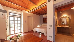 A bedroom with a bed, a wooden table with a vase, a bathroom with a sink and mirror, and a door leading to another room. - Charming studio with all amenities in stone house-Tuscany, 8 miles from Florence (Toscana)