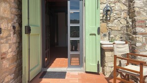 A stone building entrance with green doors, a tiled patio, and a wooden chair. - Charming studio with all amenities in stone house-Tuscany, 8 miles from Florence (Toscana)