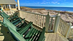 Une terrasse couverte, dotée de bancs verts, offre une vue sur une plage accessible par une promenade en bois.