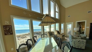 Un vaste espace dédié à la salle à manger, avec une grande table en verre et des chaises, donnant sur une plage.