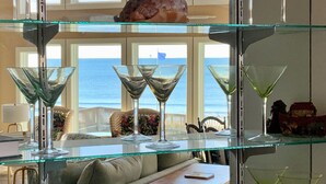 Une étagère en verre sur laquelle sont posés des verres à martini et un coquillage, avec vue sur une plage.