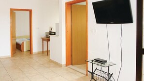 Habitación de hotel con cama, una mesita con lámpara, televisor montado en la pared y un carrito con cables.