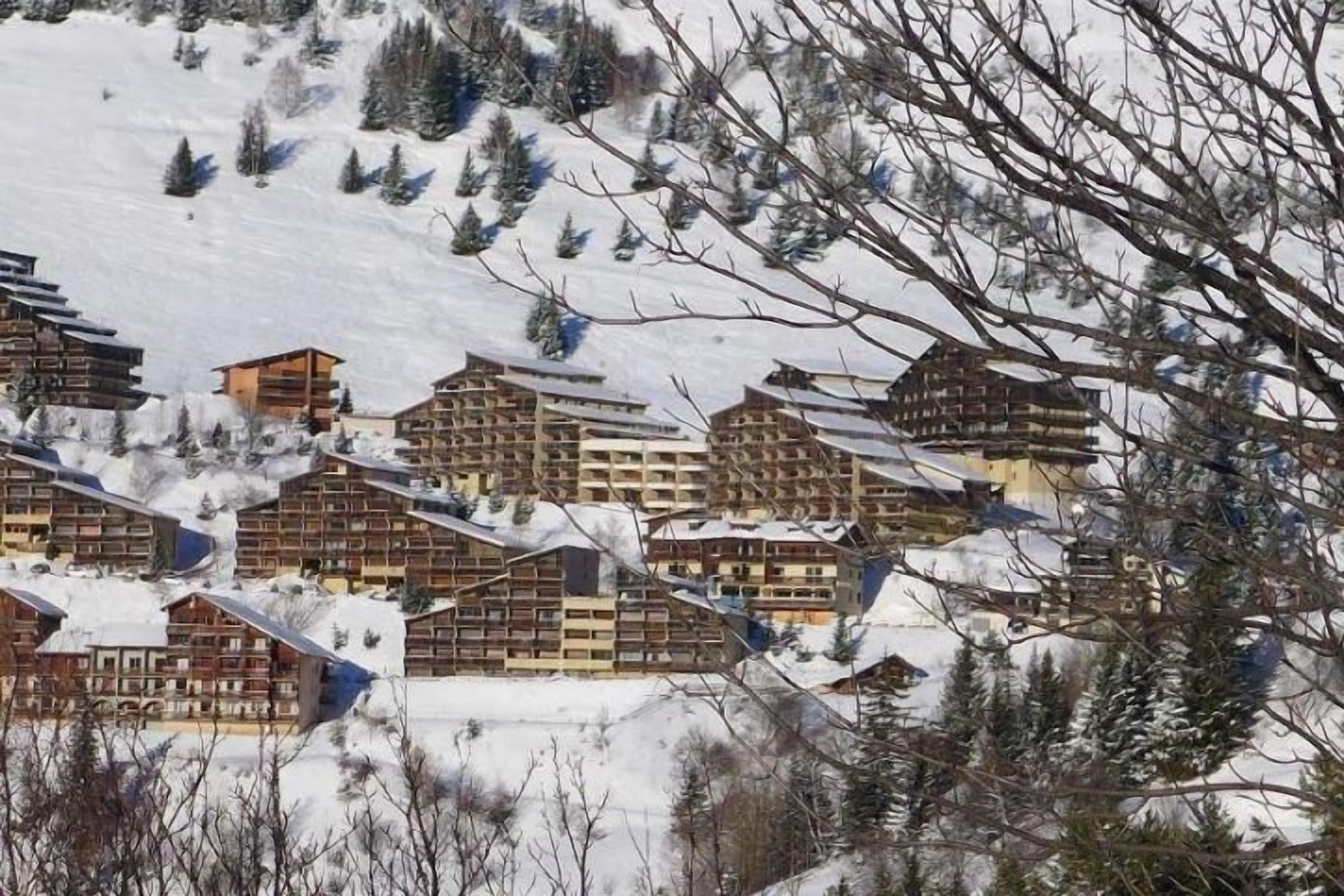 A cluster of chalet-style buildings with multiple floors, surrounded by snow-covered terrain and sparse trees.