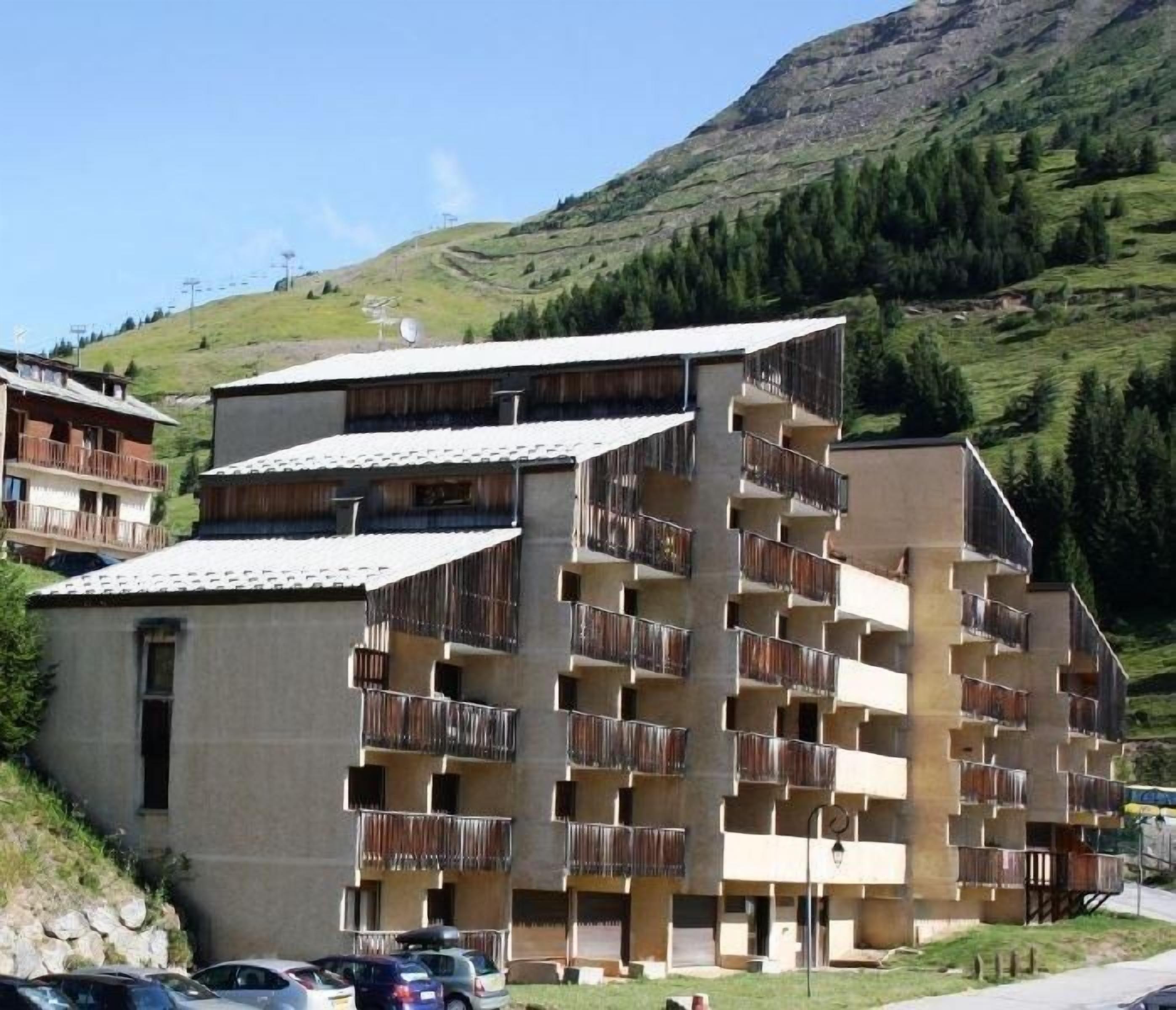 Un hôtel à plusieurs étages, doté de balcons, situé dans une région vallonnée sous un ciel dégagé.